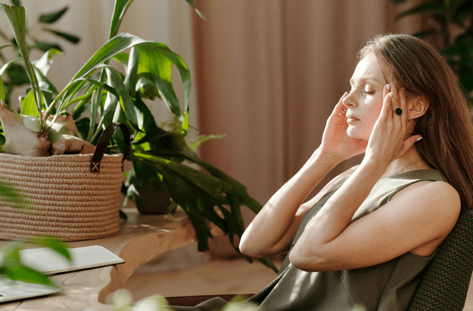A young woman sits, holding her temples and appears to be in pain.