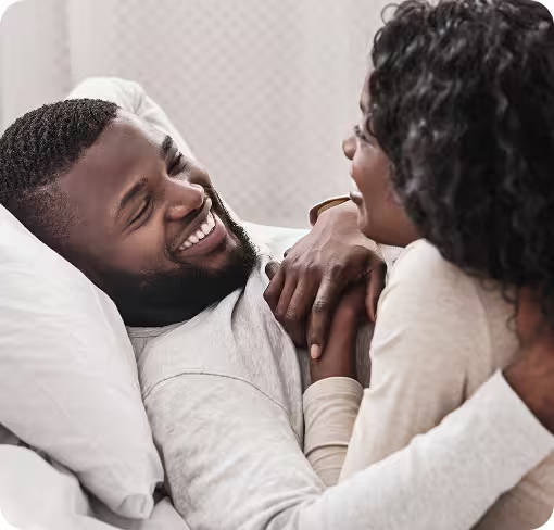 Ein lächelndes Paar liegt entspannt im Bett, was Entspannung durch medizinisches Cannabis andeutet.