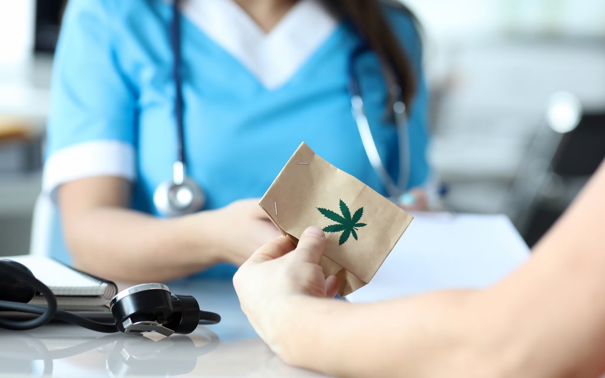 Ärztin übergibt einem Patienten eine Packung mit dem Symbol eines Cannabisblattes.