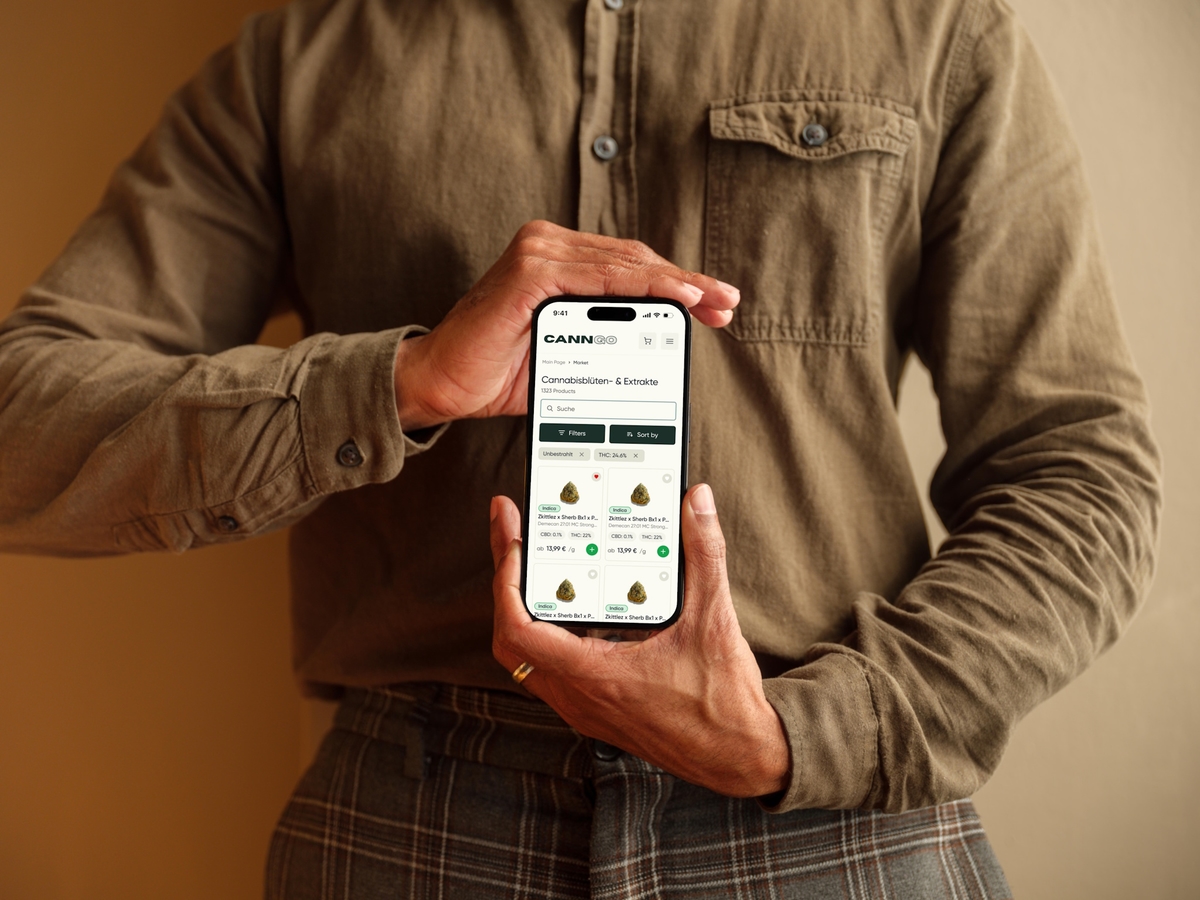 Mann in Khaki-Shorts hält iPhone mit geöffnetem CannGo-Markt