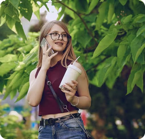 Young woman talking on the phone outside with a drink, cannabis infusion, in her hand.
